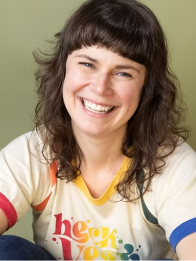 smiling woman with brown, long hair and cream top with rainbow trim