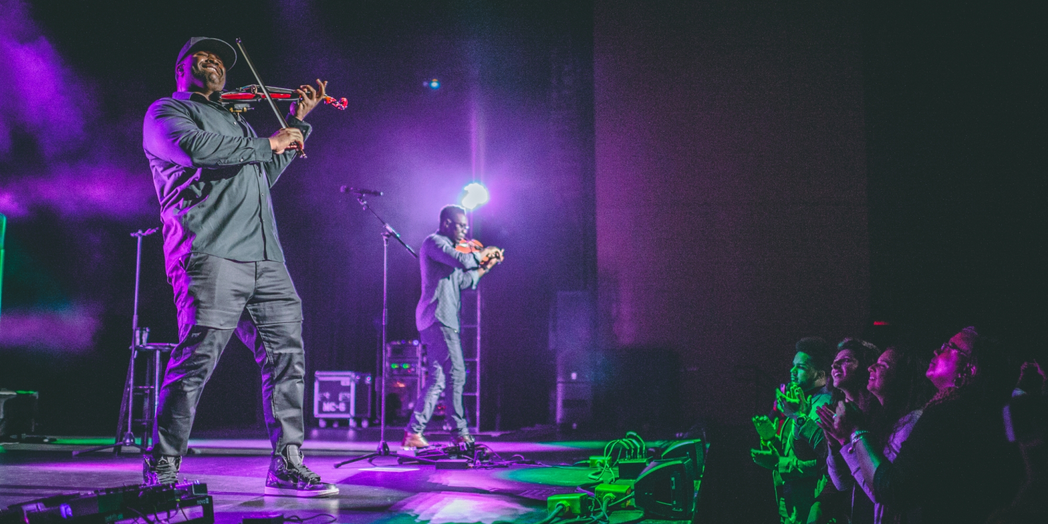 Image of the artists from Black Violin on stage at the Lied Center lit in purple light in front of a crowd of UNL students