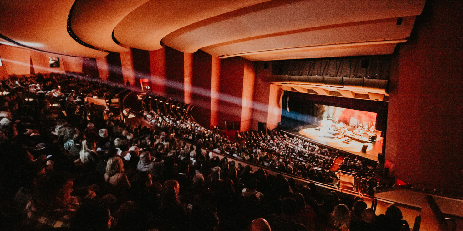Crowd in theater seats with spotlights on the stage.